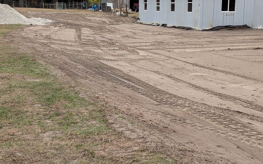 A compacted sand building pad graded alongside a new white metal building